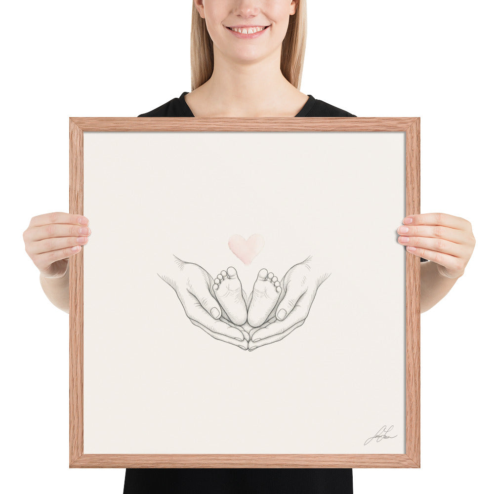 Ten Little Toes, a fine-line drawing of a parent's hands cradling a baby's feet beneath a small blush heart, Beloved print by Jamie Lawrence in a Red Oak frame, held to show scale